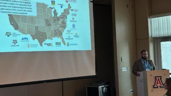 A man presenting behind a podium beside a projection of a map of the U.S.
