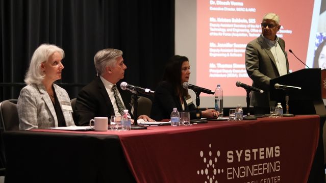 Three government officials at a desk with microphones and one scientist at a podium